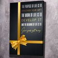 Black canvas wall art with gold stripe, quote text, and gold gift ribbon bow.