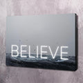 Motivational wall art canvas with glowing 'BELIEVE' over ocean waves, black frame